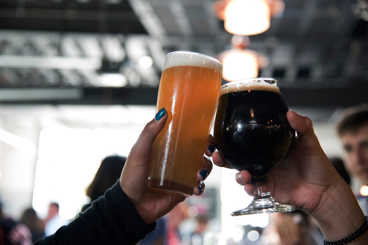 Two hands clink glasses of different craft beers, capturing a celebratory moment in a modern bar.